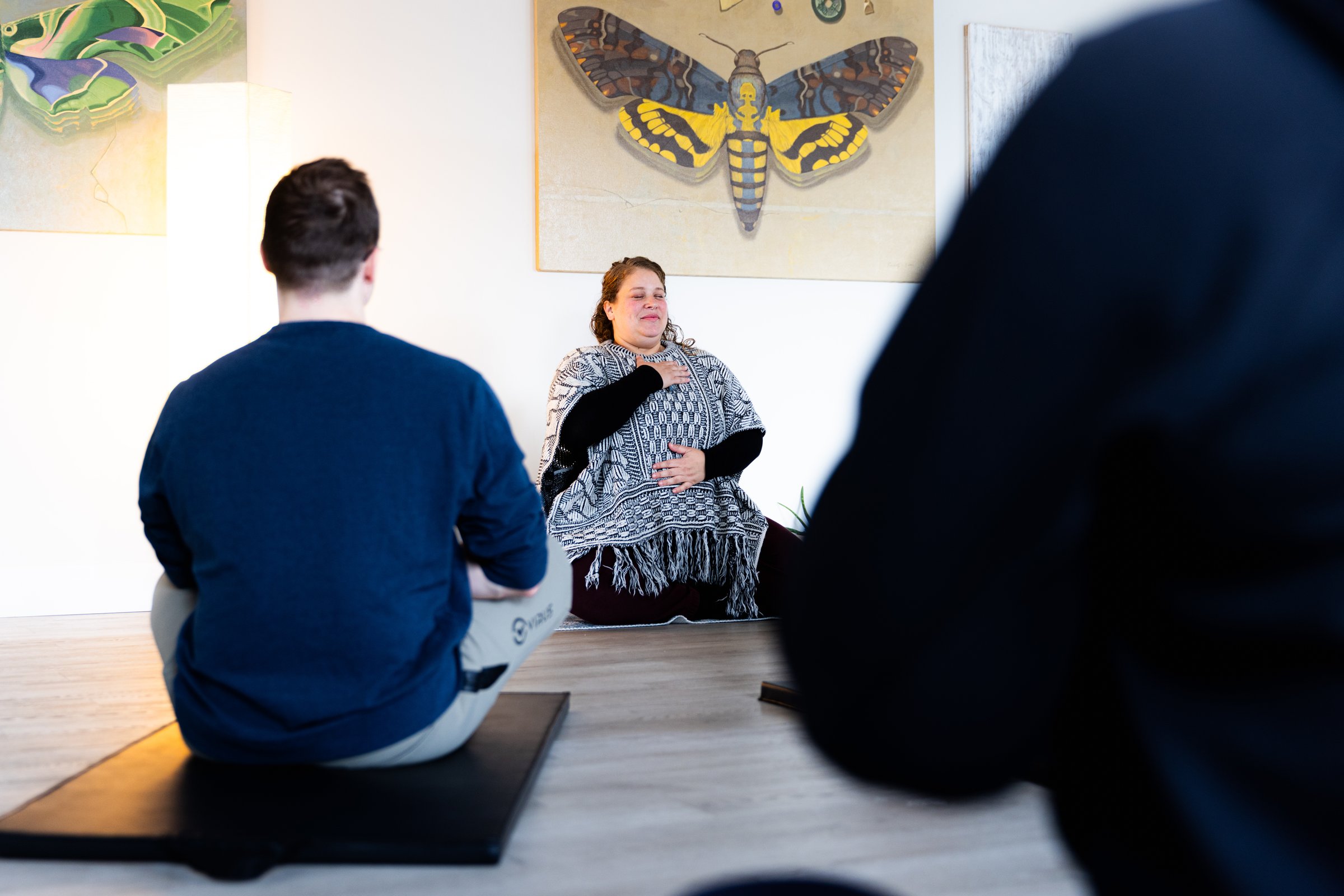 A somatic instructor leading a seated group, one hand on her chest